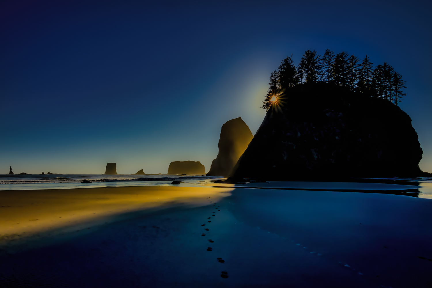 Beach sunset with a sunstar shining in a sea stack with light glowing on the sandy Second beach of the Pacific ocean. Additionally...